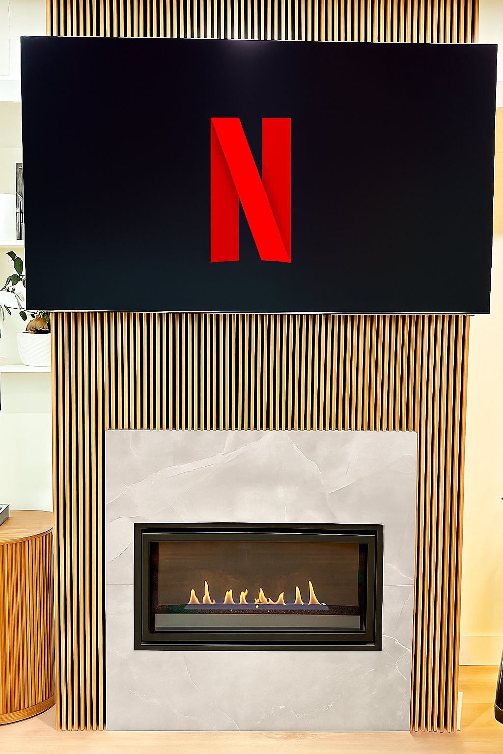 Flat-screen TV displaying Netflix logo mounted above a modern fireplace with vertical wooden slat surround and white marble backdrop