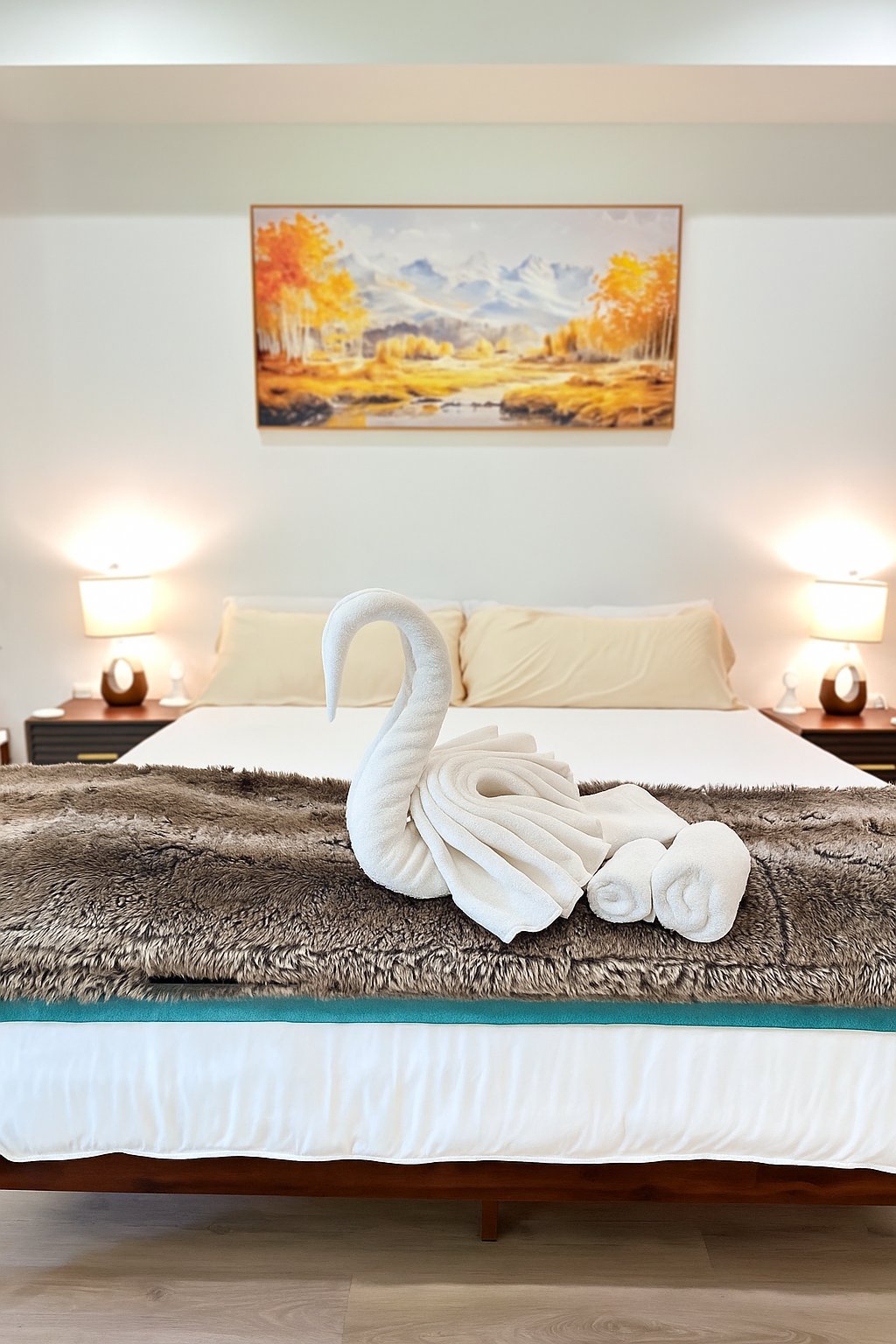 Hotel bedroom with decorative white towel swan sculpture on bed, landscape painting above headboard, and bedside lamps