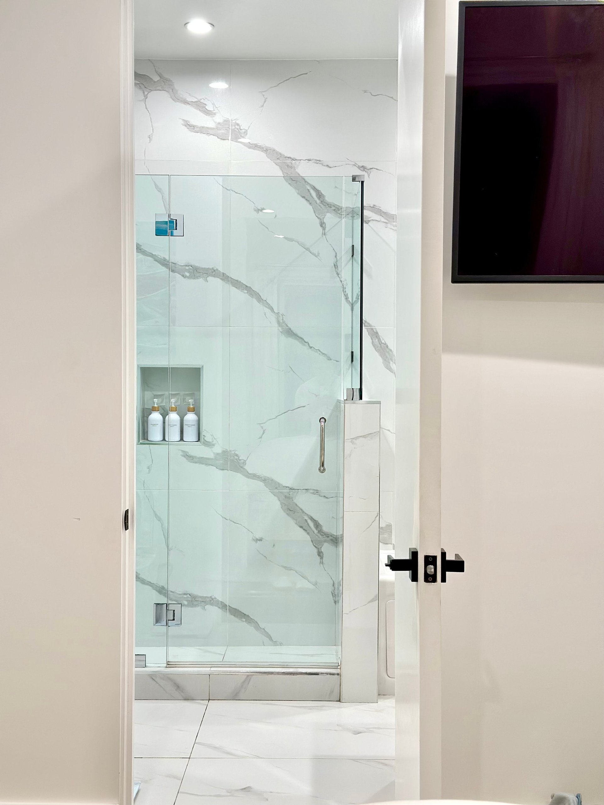 Modern bathroom shower enclosure with marble tile walls and glass door in a white tiled floor bathroom