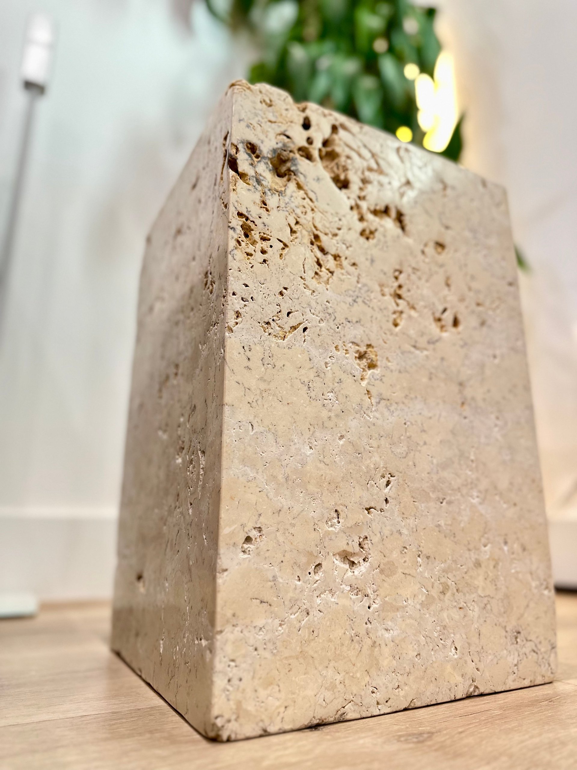 Beige concrete or stone planter with textured porous surface on wooden table with blurred green plant in background