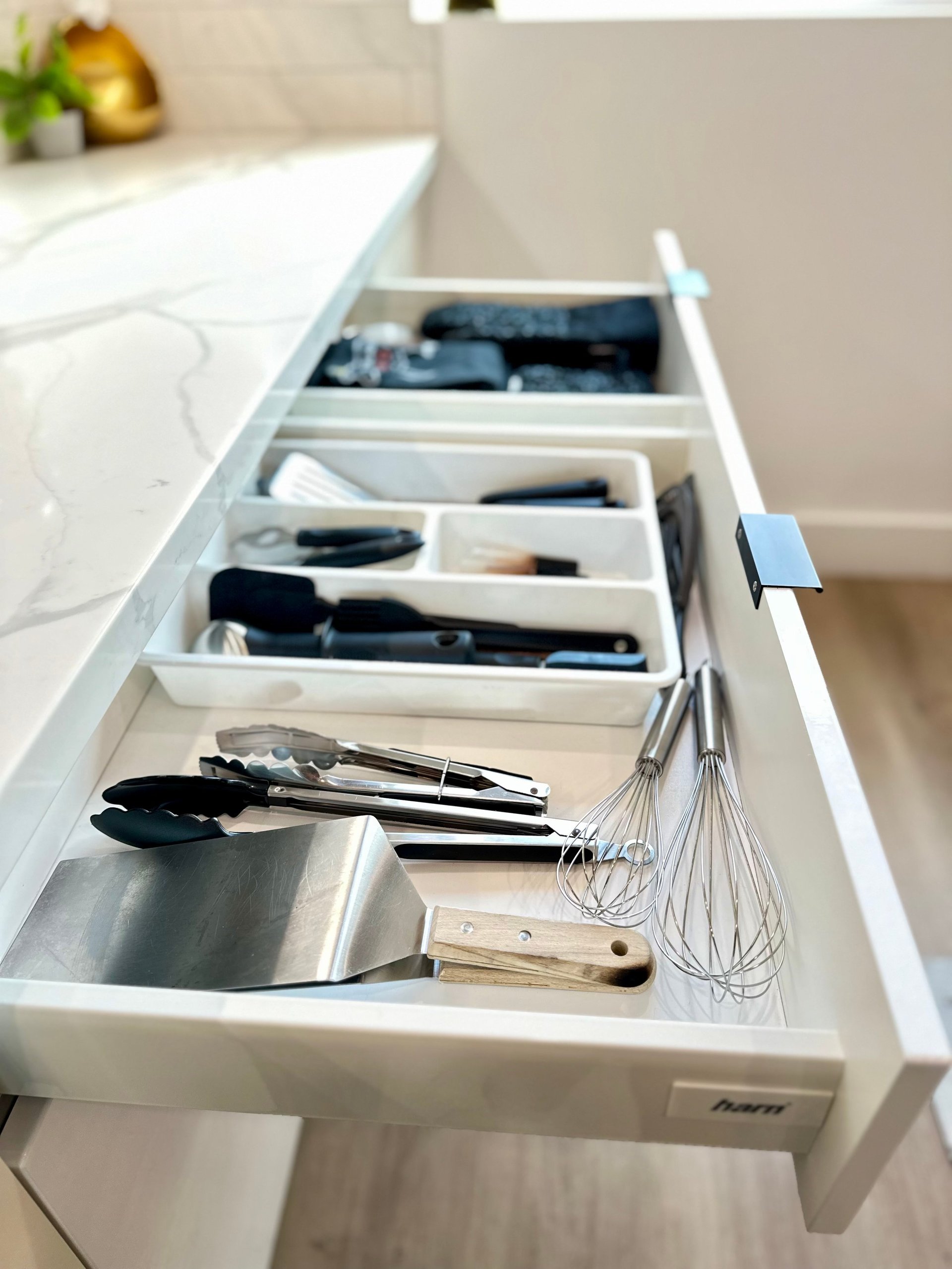 Organized kitchen drawer with dividers containing cooking utensils including spatulas, whisks, tongs, and wooden spoons