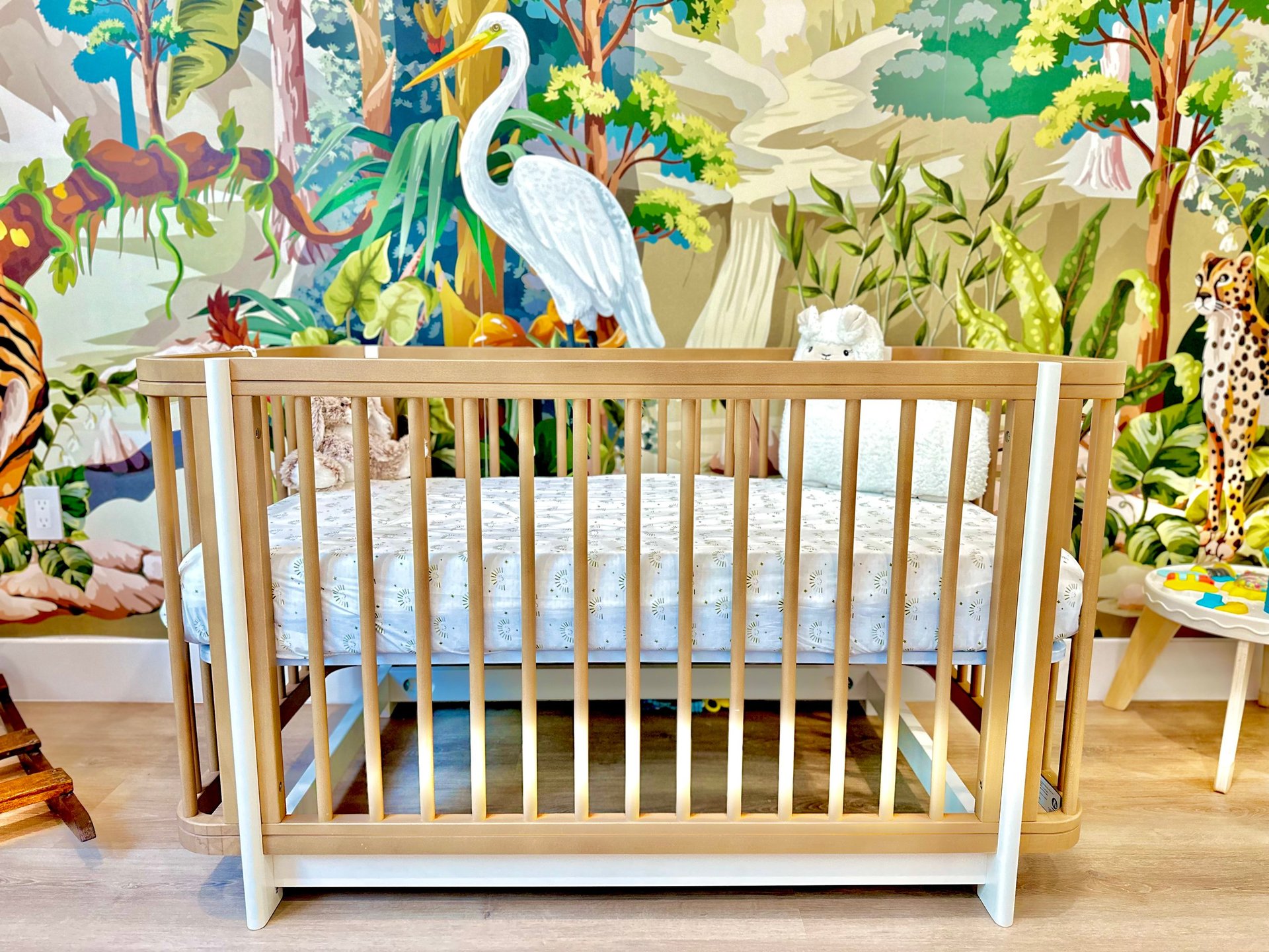 Wooden crib in a nursery with vibrant jungle animal wallpaper and matching decor