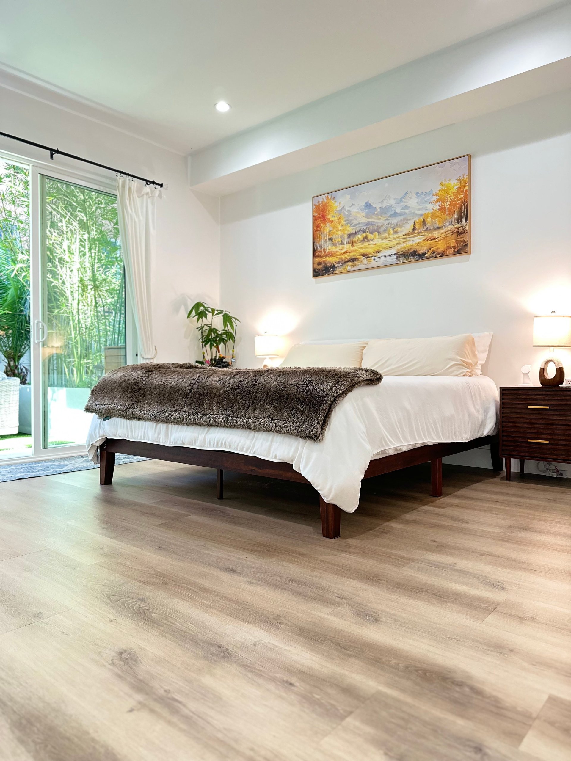 Modern bedroom with dark wood bed, white bedding, wooden nightstands, glass doors opening to garden, and landscape artwork on wall