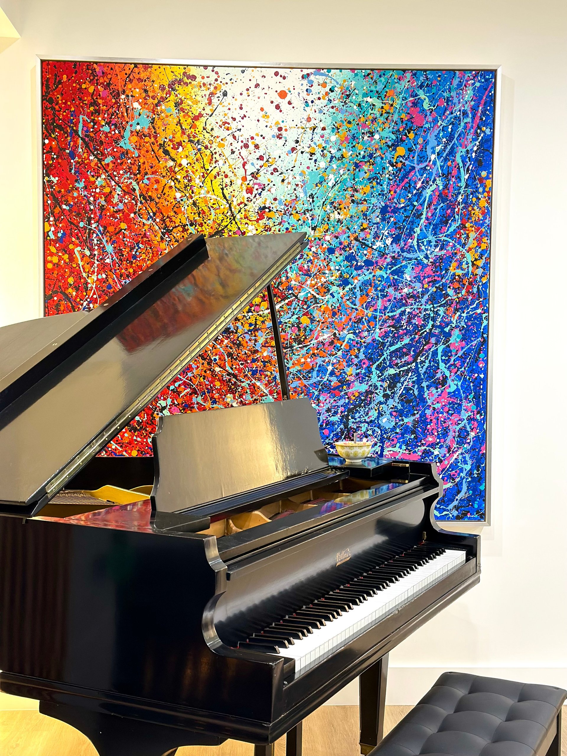 Black grand piano in front of a vibrant abstract painting with splattered colors ranging from red to blue