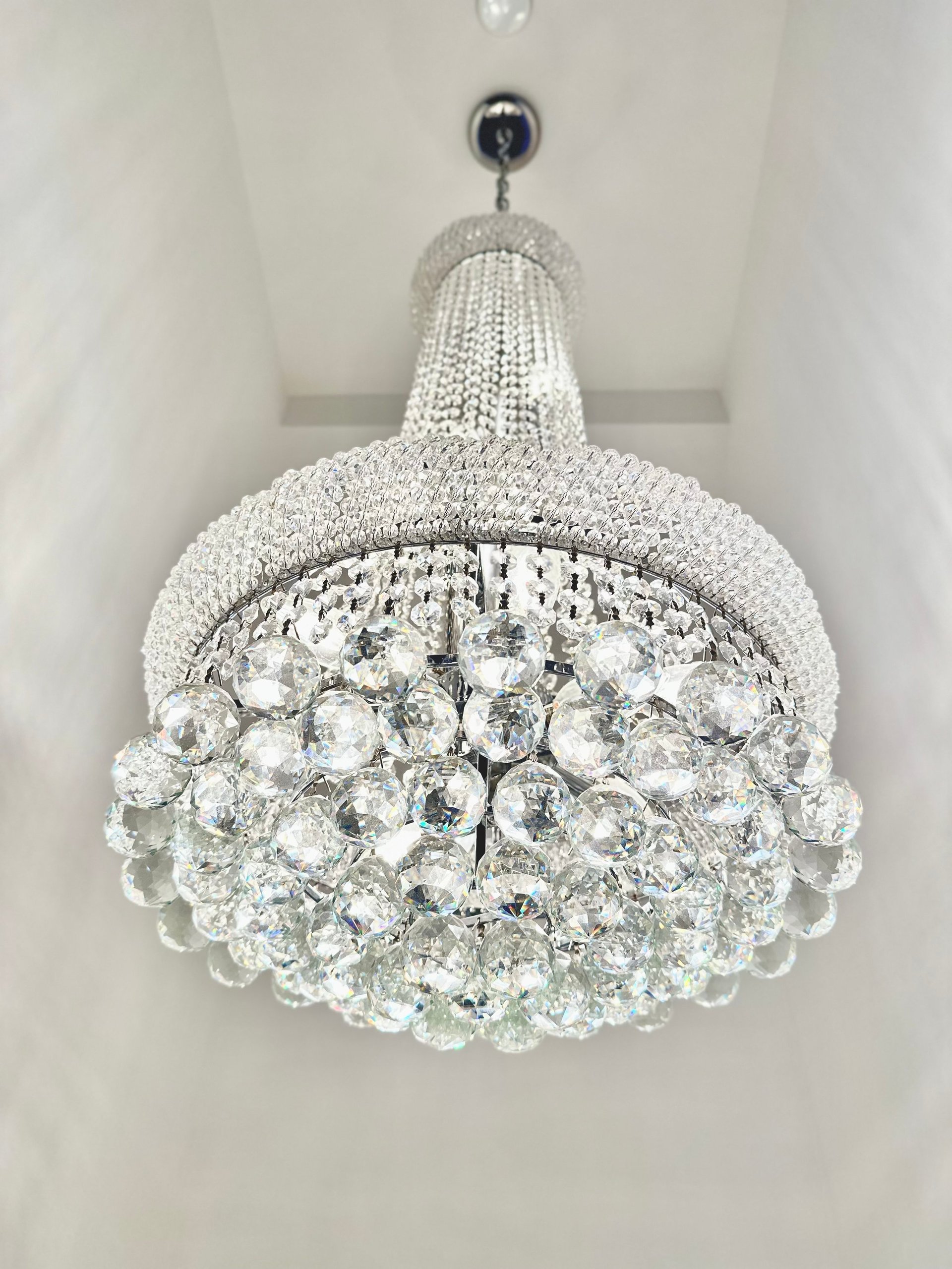 Crystal chandelier with spherical crystal drops hanging from a beaded metal frame, mounted on a white ceiling