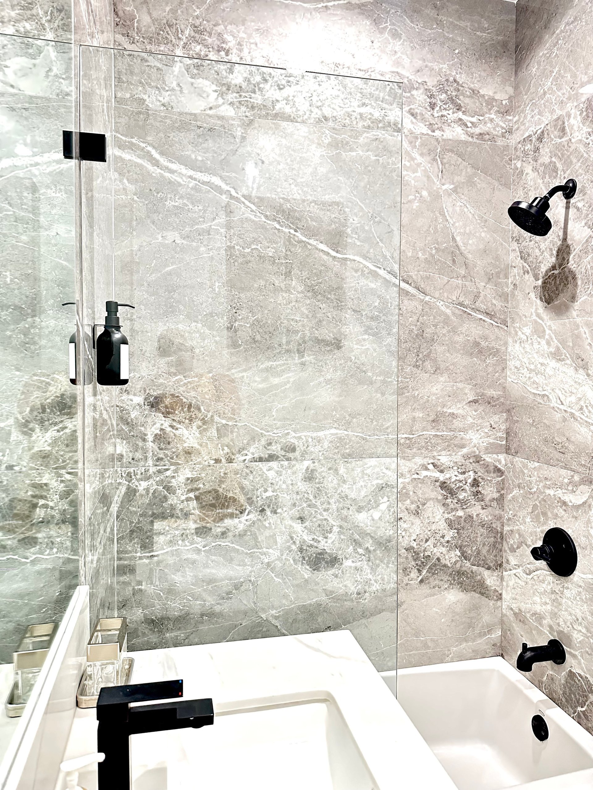 Modern bathroom with marble tile shower enclosure, white soaking tub, black fixtures, and glass shower door
