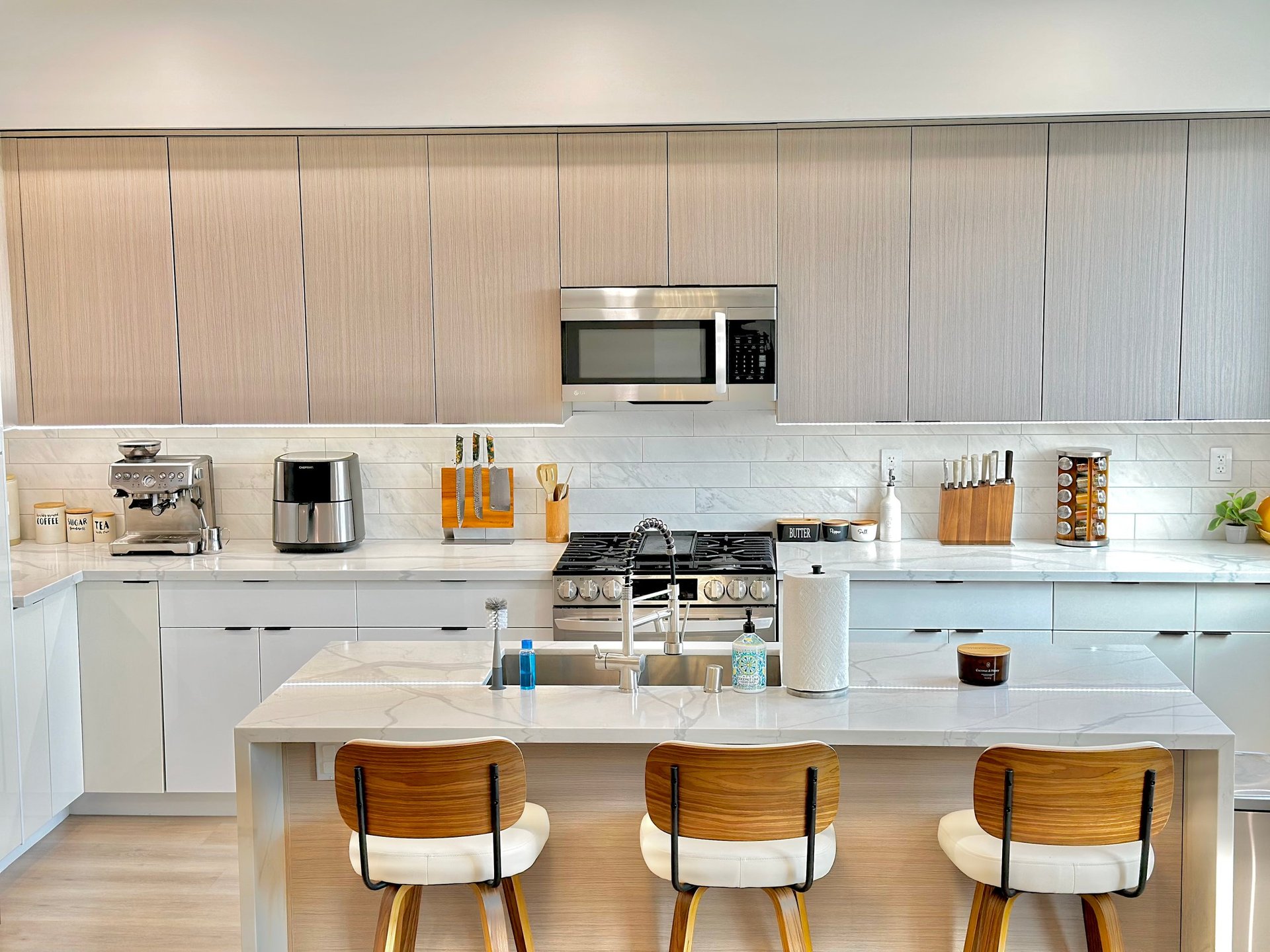 Modern kitchen with white cabinetry, white subway tile backsplash, wood grain ceiling, island with three wood chairs, and stainless steel appliances