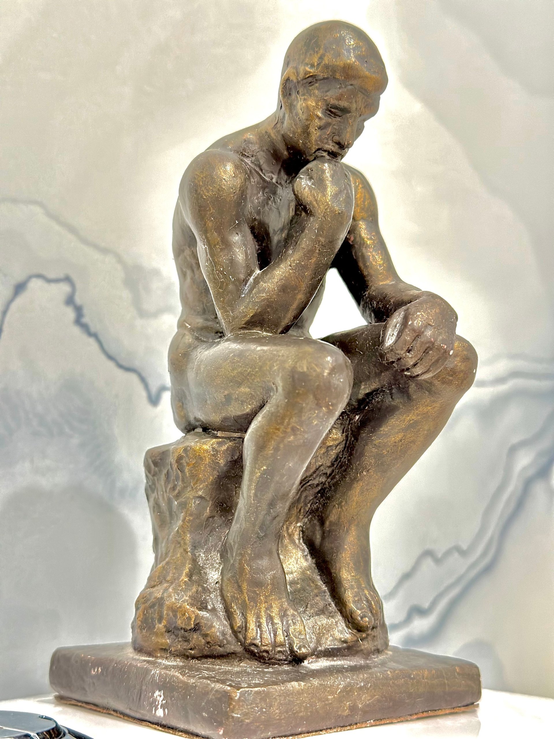 Bronze sculpture of a nude male figure in a contemplative seated pose with hand to face, mounted on a rectangular base